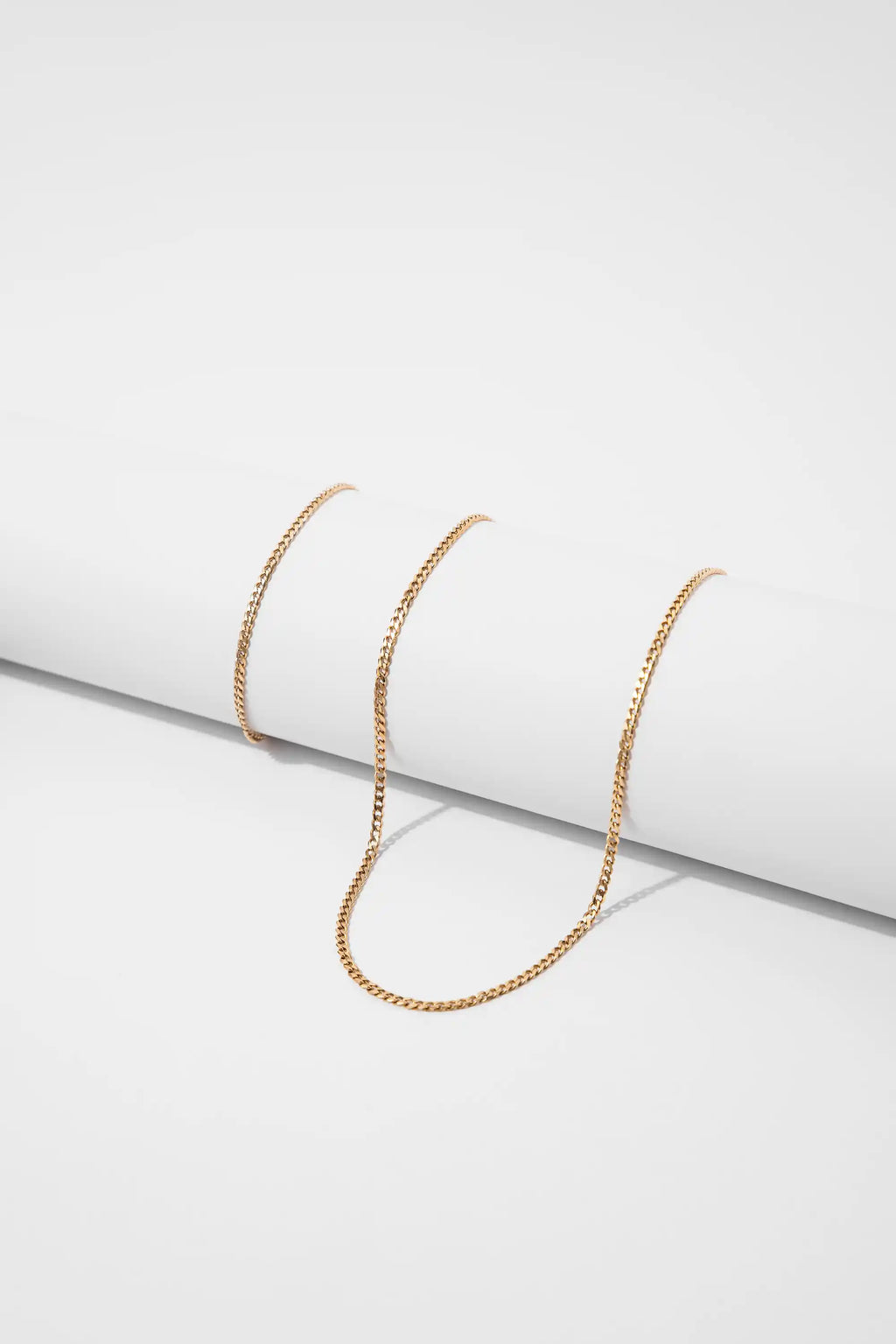 Pulsera Cubana Gold Impetu Men - cadena cubana enrollada sobre prop blanco vista lateral