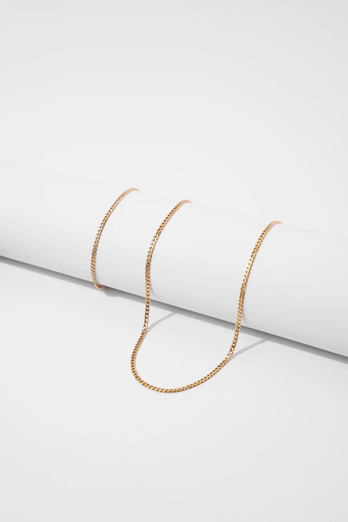 Pulsera Cubana Gold Impetu Men - cadena cubana enrollada sobre prop blanco vista lateral